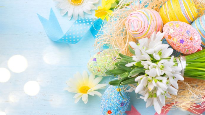 Pastel Easter eggs with flowers and a blue ribbon on a light blue wooden surface