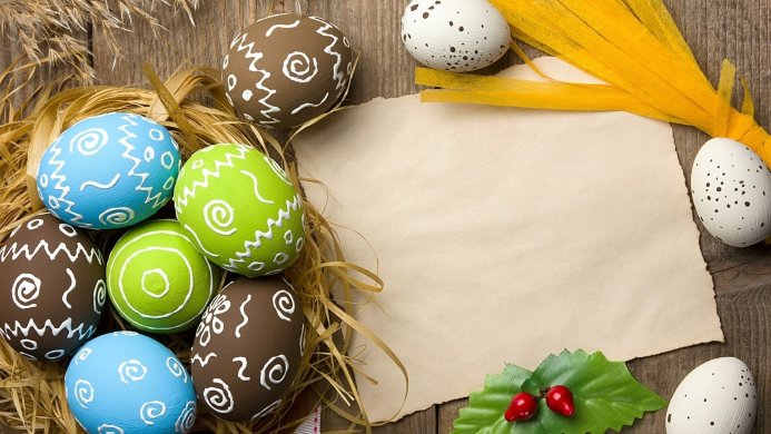 Colorful Easter eggs with patterns, yellow straw and blank card on a wooden table