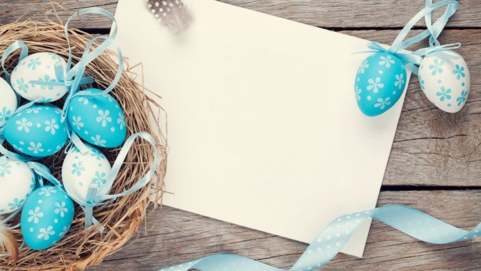 Easter eggs in a nest with a feather and a blank card on a wooden table