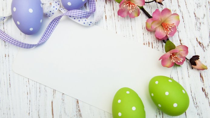Easter eggs, ribbon, flowers and a blank card on a wooden background