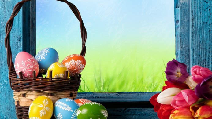 Easter basket with decorated eggs and tulips by a window
