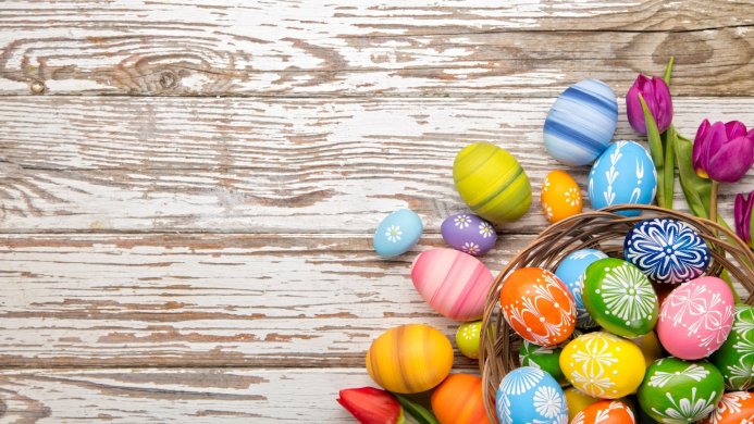 Colorful Easter eggs in a basket with tulips on a weathered wooden surface