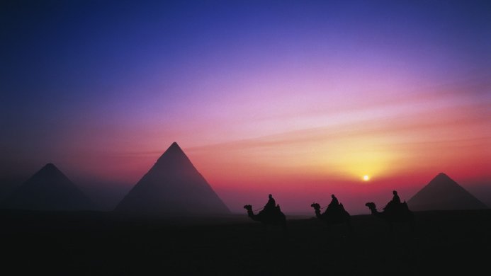 Silhouette of pyramids and camel riders at sunset in Egypt