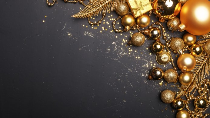 Gold Christmas ornaments, a gift box, and glitter on a dark background
