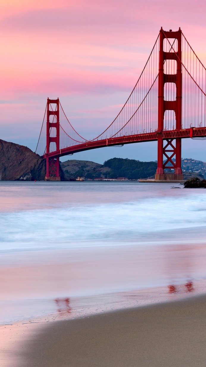 Golden Gate Bridge at sunset with pink sky and ocean waves