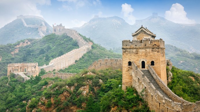 The Great Wall of China winding through a green, mountainous landscape under a cloudy sky
