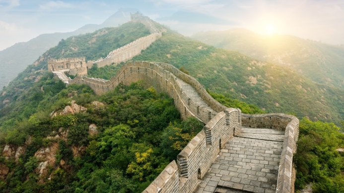 The Great Wall of China winds through green hills under a bright sun