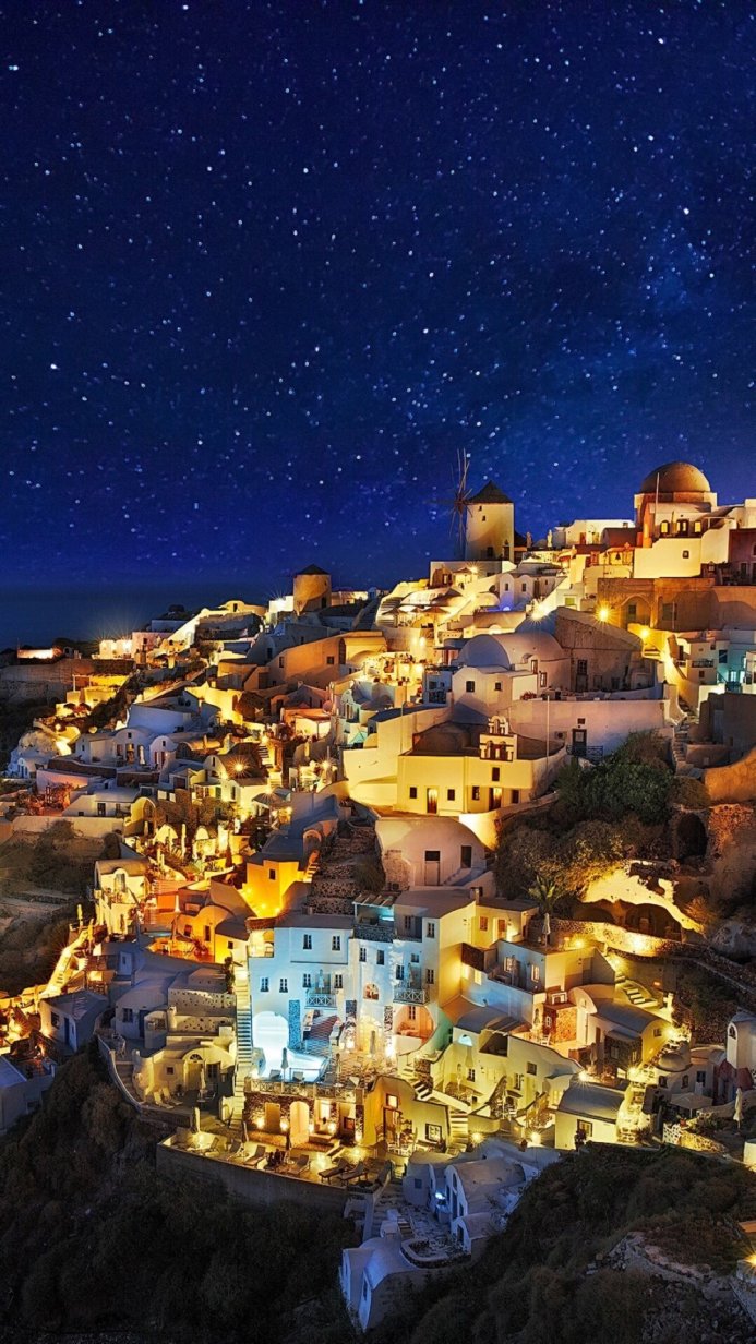 Night view of a greek village with a windmill, white buildings on a hill under a starry sky