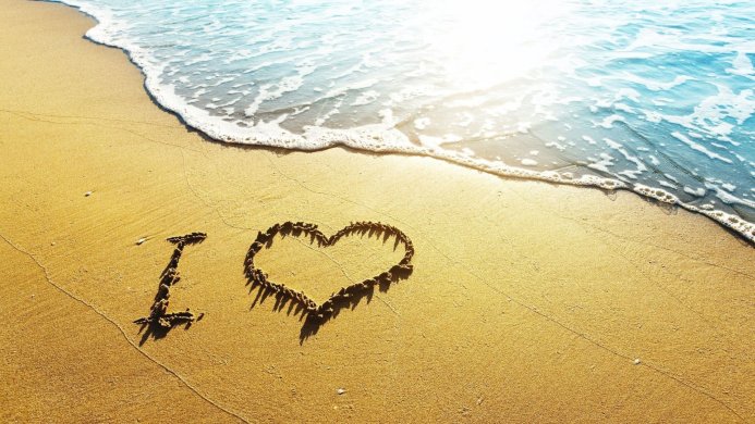 I love heart symbol written on golden sand beach with soft ocean wave in the background