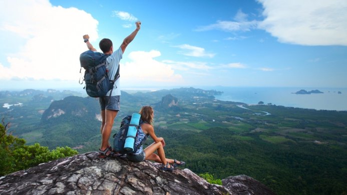 Two hikers on a mountain peak overlooking a lush valley and ocean view