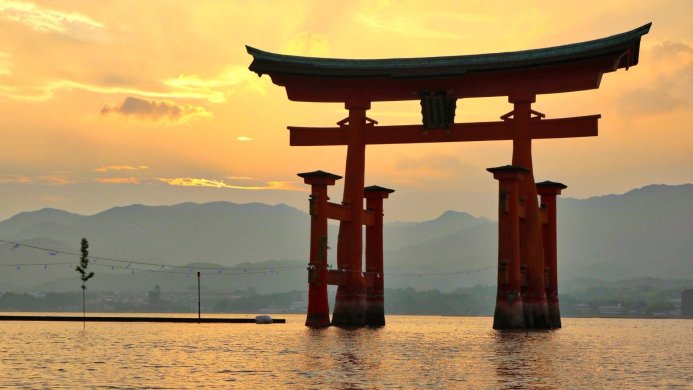 Itsukushima Torii Gate at sunset in Japan with mountains in the background
