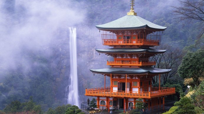 Japanese pagoda with a waterfall in the background, surrounded by green trees