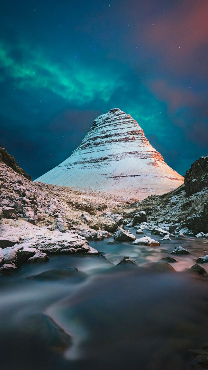 Snow-covered mountain under the aurora borealis with a stream in the foreground