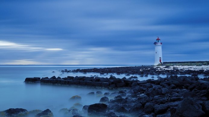 White lighthouse on a rocky shore under a cloudy blue sky