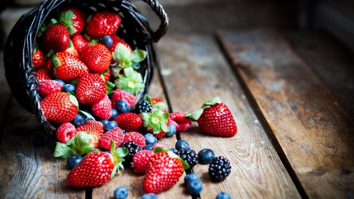A basket of fresh strawberries, raspberries, blueberries and blackberries on a wooden table