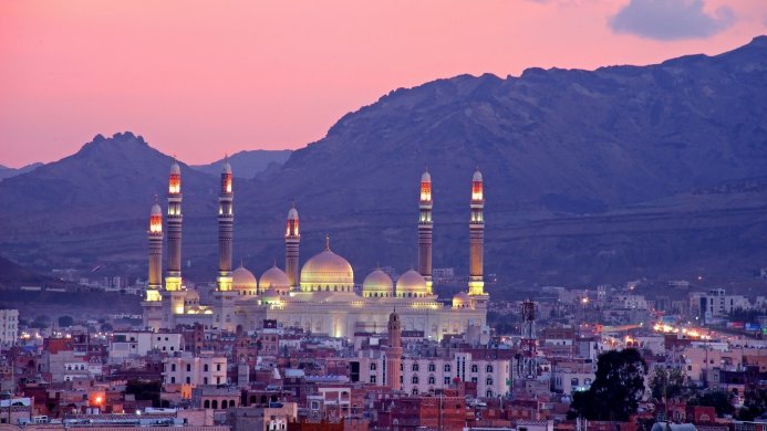 A mosque with minarets at sunset, against a mountain backdrop, in a city