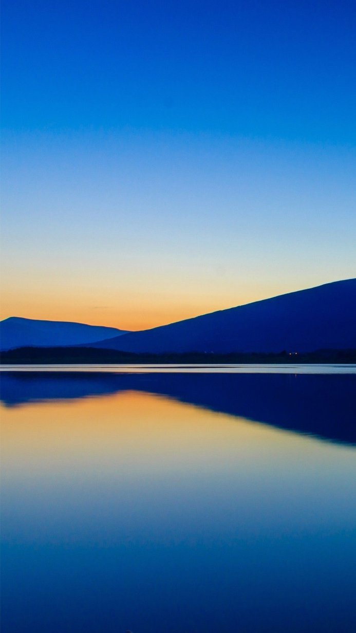 Mountains reflecting in a calm lake under a clear sky at dusk
