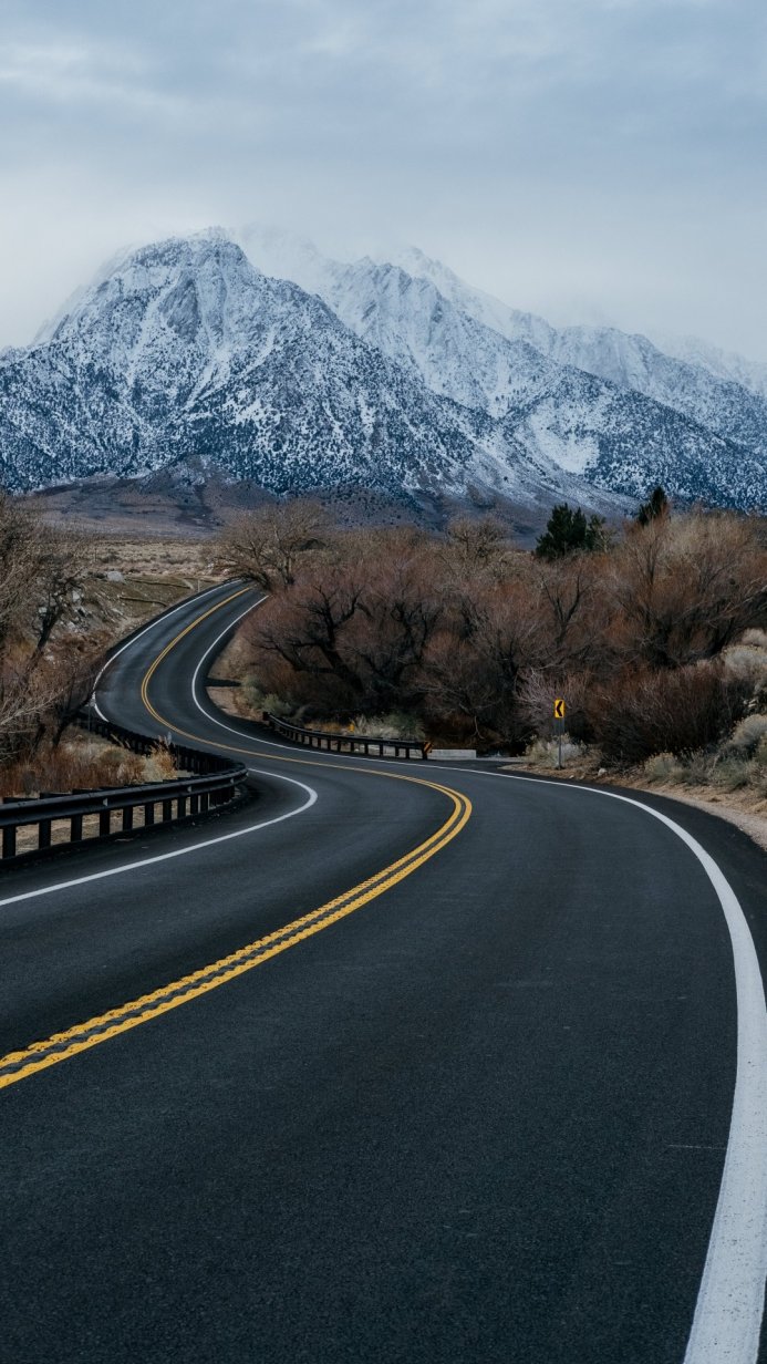 Curving road leading to snow-covered mountains under a cloudy sky