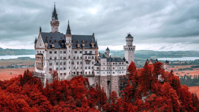 Neuschwanstein Castle in Bavaria, Germany, surrounded by red autumn trees, under a cloudy sky