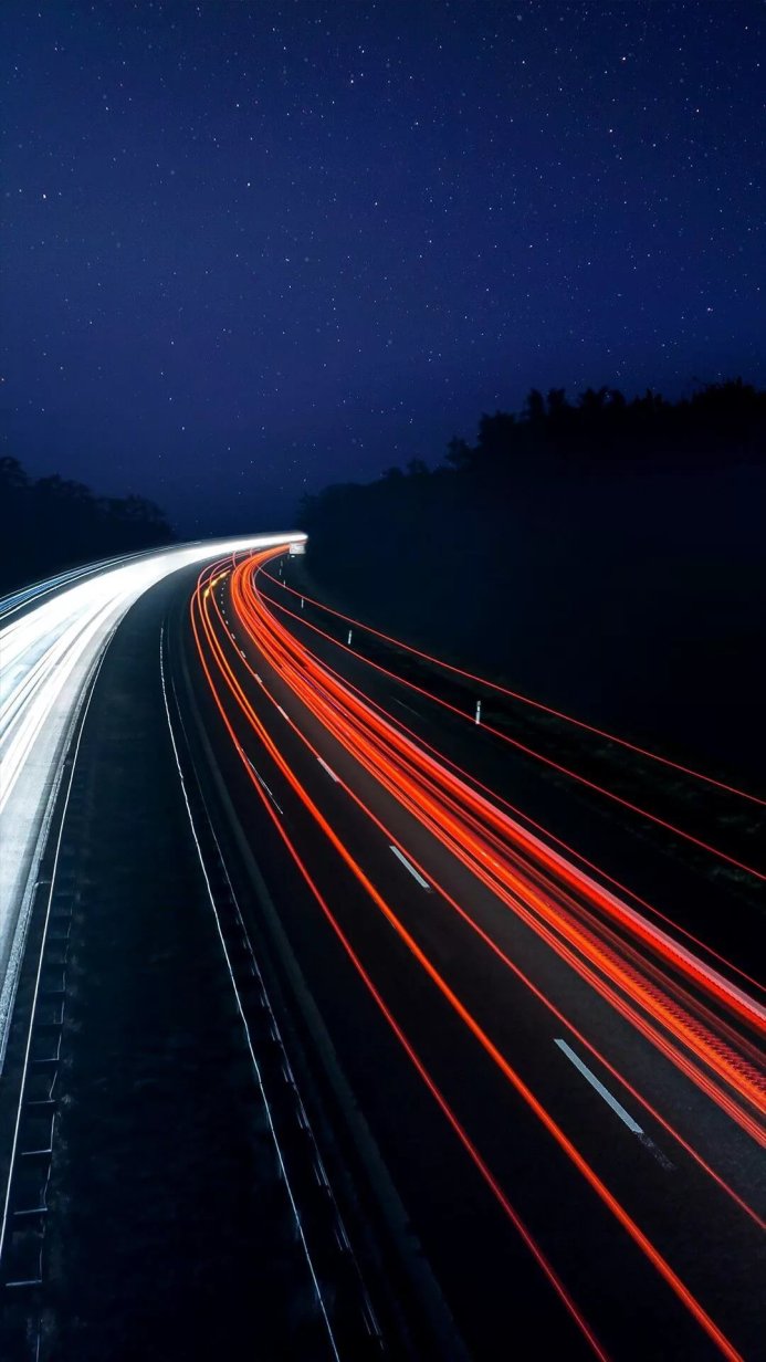 A highway at night with car light trails under a starry sky