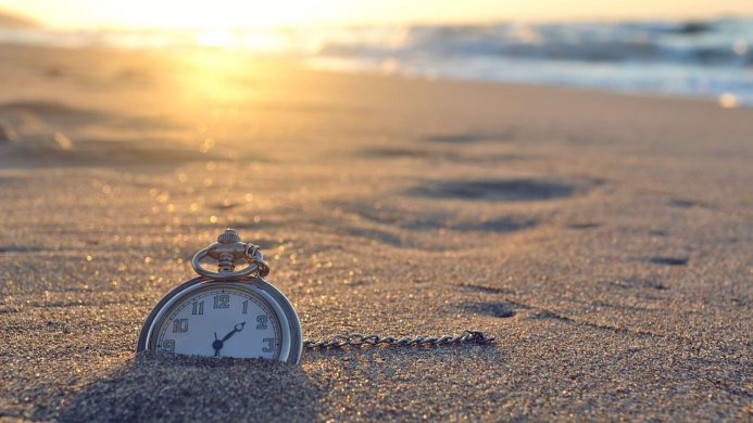 A pocket watch partially buried in the sand on a beach at sunset