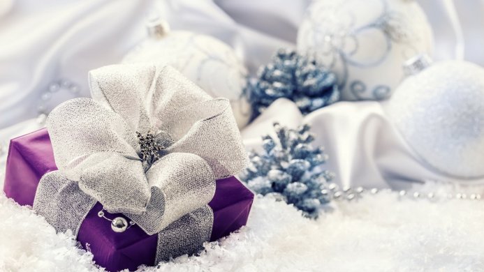 A purple gift box with silver bow, christmas ornaments, pine cones, and snow decorations
