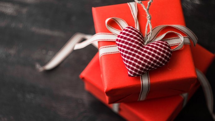Stack of red gift boxes with a heart ornament and ribbon on a dark wooden background