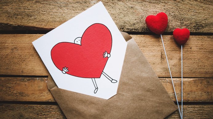 Red heart drawing in an envelope with small red heart decorations on a wooden background