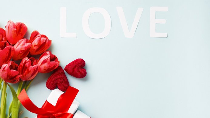 Red tulips, knitted hearts, and a gift with LOVE letters on a light blue background