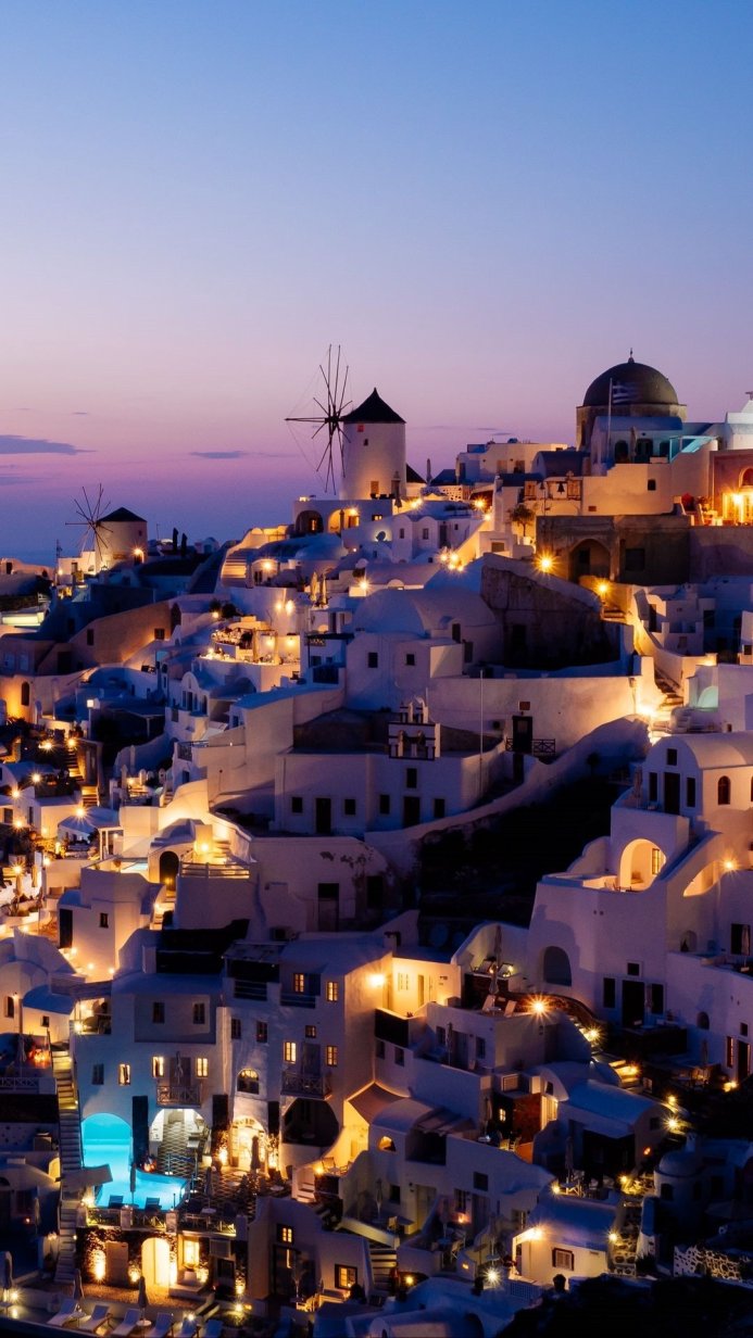 White houses and windmills of Santorini, Greece, at night under a purple and blue sky