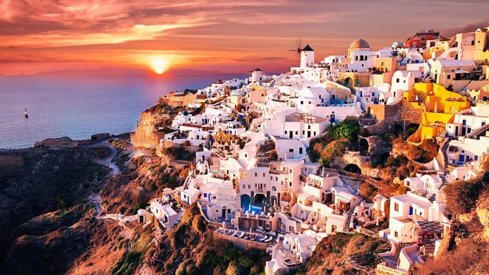 Santorini, Greece at sunset with white buildings and a windmill overlooking the sea