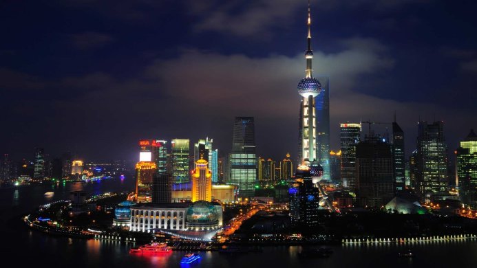 Shanghai cityscape at night with brightly lit skyscrapers and a river