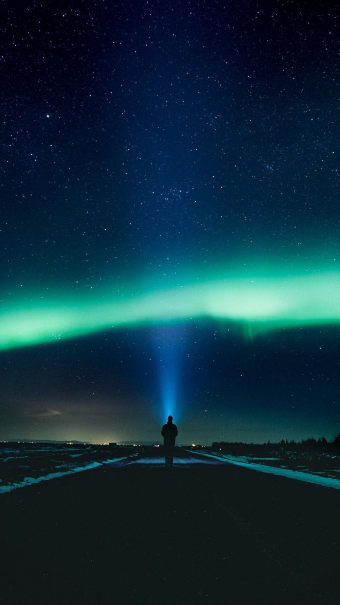Silhouette under aurora borealis with starry sky. A person illuminates the sky with a ray of light