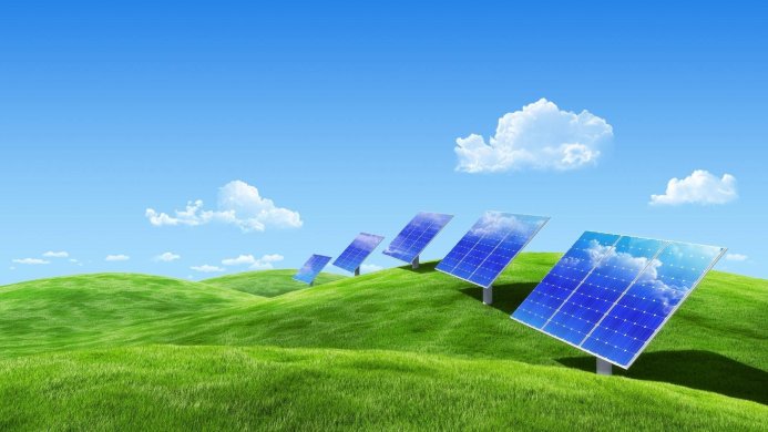 Solar panels in a green field with a blue sky and clouds