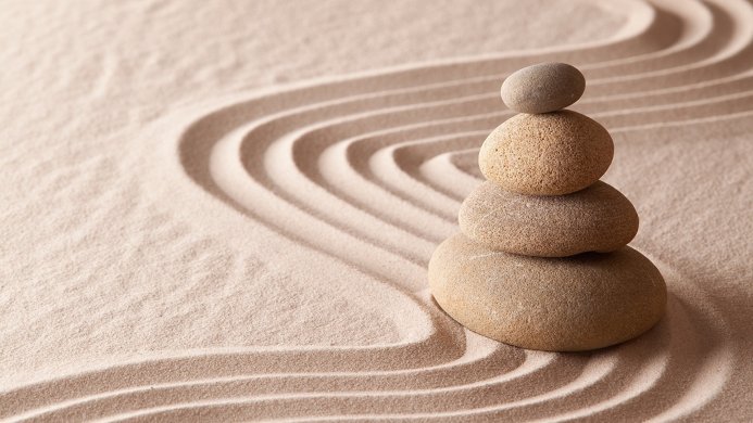 A stack of four stones on raked sand in a zen garden