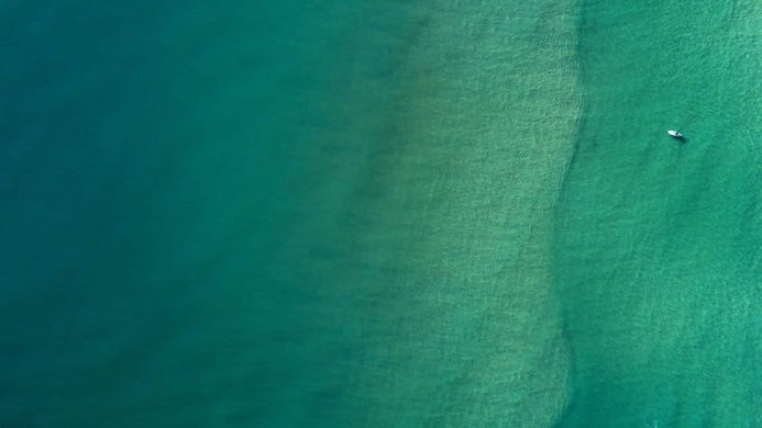A lone surfer in the turquoise ocean, seen from above