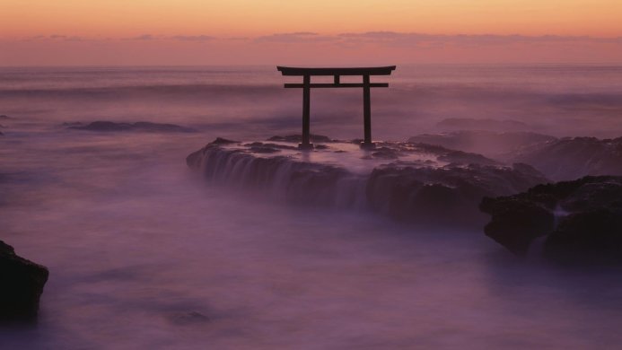Torii gate silhouette on a rocky outcrop at sunset in a tranquil seascape scene