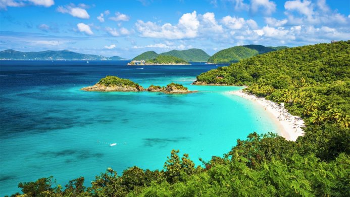 Turquoise water and a white sand beach with lush green hills in the background on a tropical island