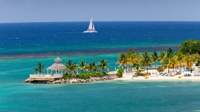 Tropical island scene with a gazebo, palm trees, a white sand beach and a sailboat on the ocean