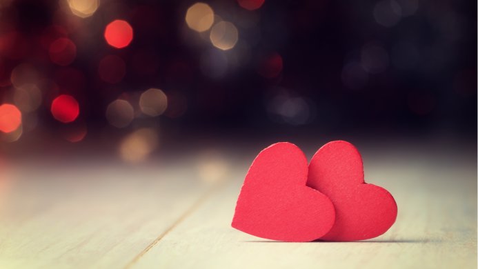 Two red hearts close together on a wooden surface, bokeh background