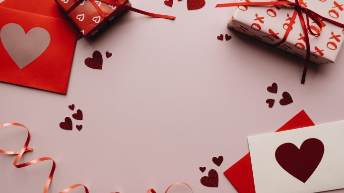 Valentine's Day themed flat lay with gifts, envelopes, heart confetti and ribbon