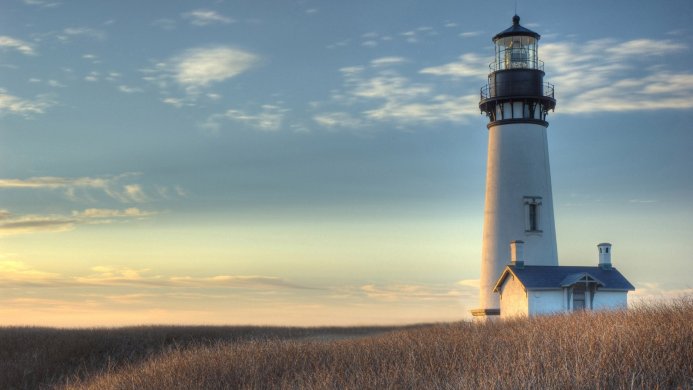 A white lighthouse on a grassy hill against a blue and golden sky