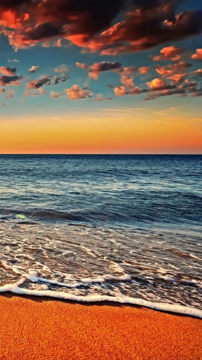 A beach meeting the sea under a colorful sky at sunset