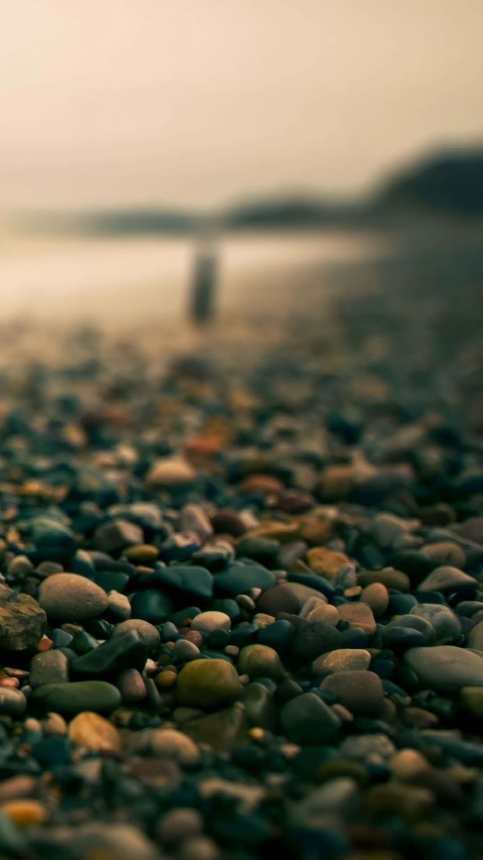 Smooth stones on a beach with water and shore in the blurred background