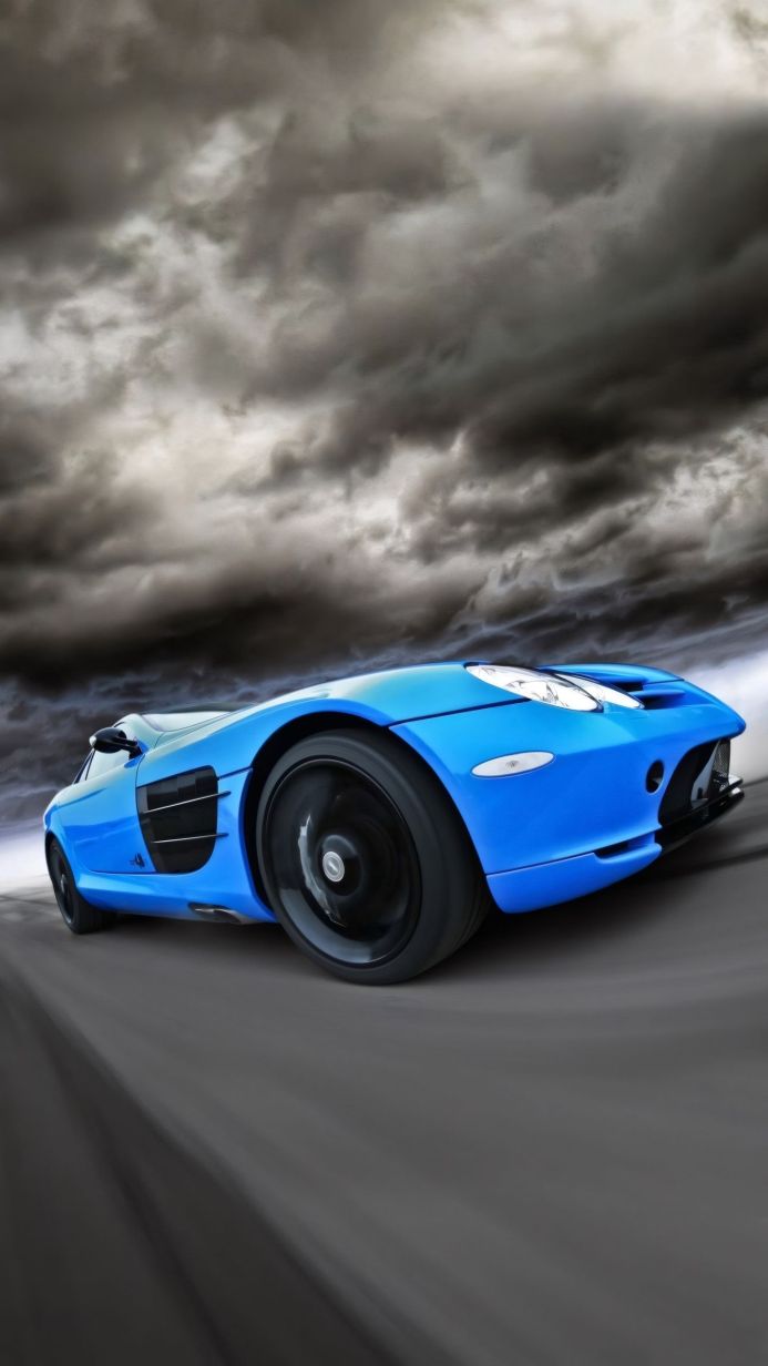 A blue sports car is driving on a road with stormy clouds in the background