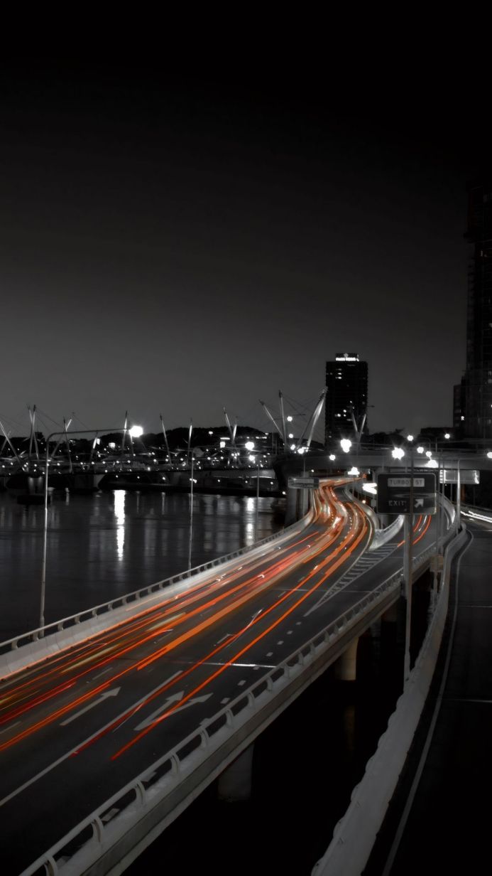 Monochrome image of a city bridge at night with blurred car light trails