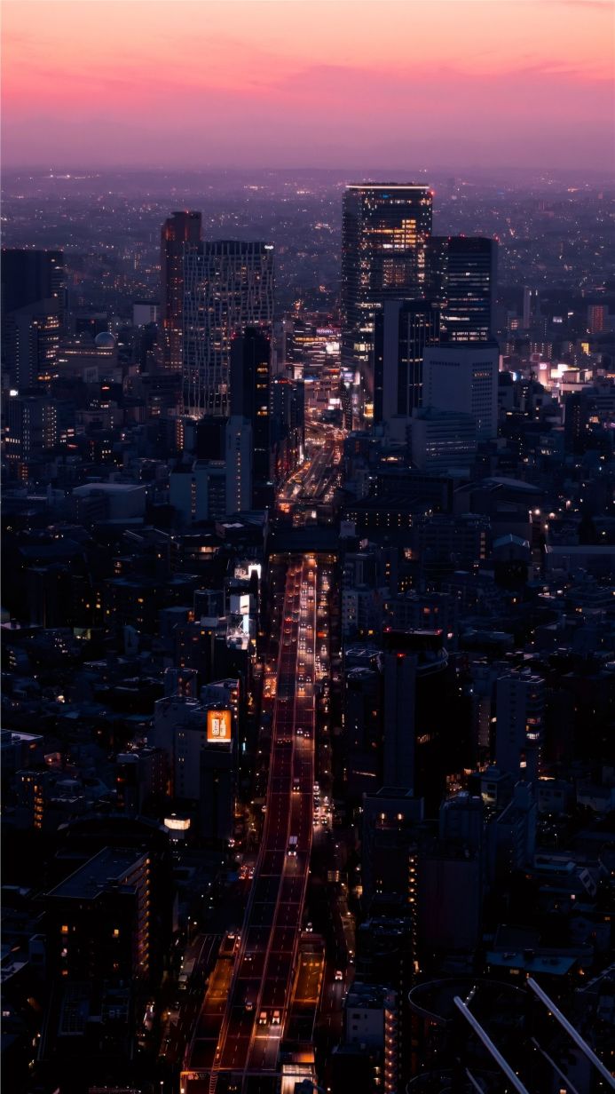 Aerial view of a city at night with purple and orange sky and illuminated buildings and roads