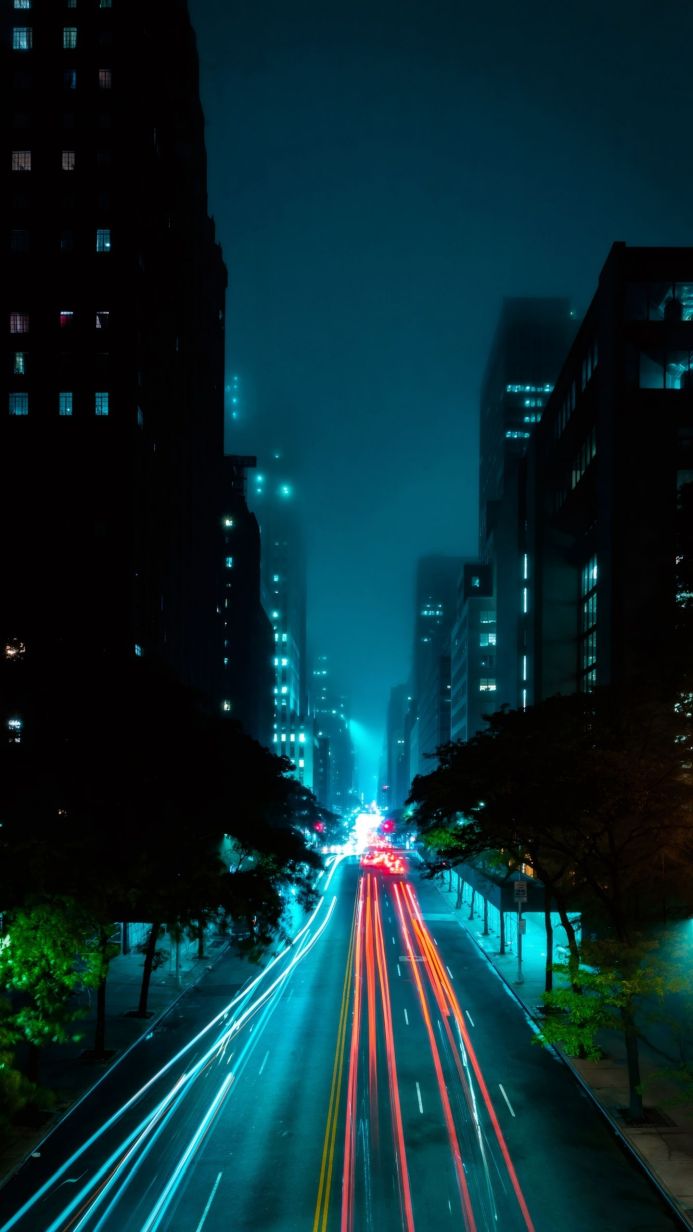 Night city street with long exposure car light trails, tall buildings, and blue hues