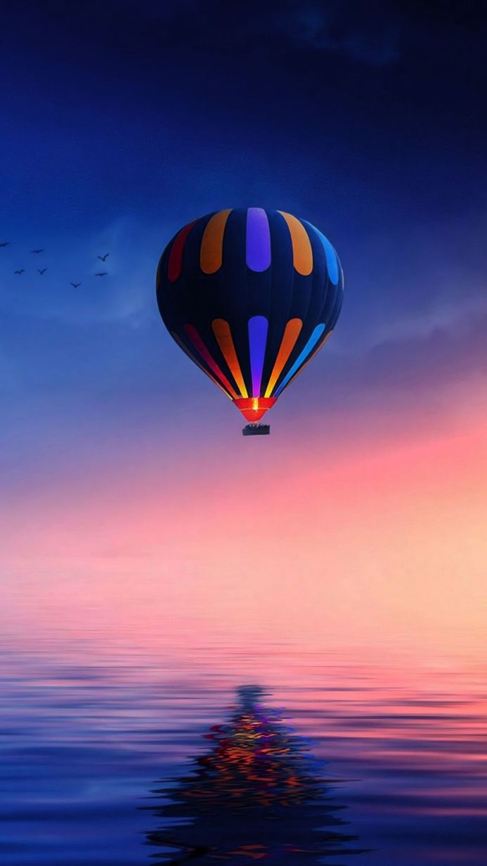 Colorful hot air balloon over water at sunset with birds flying in the sky