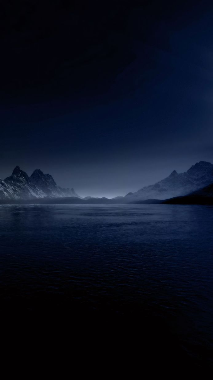 A dark lake with mountains in the background under a night sky